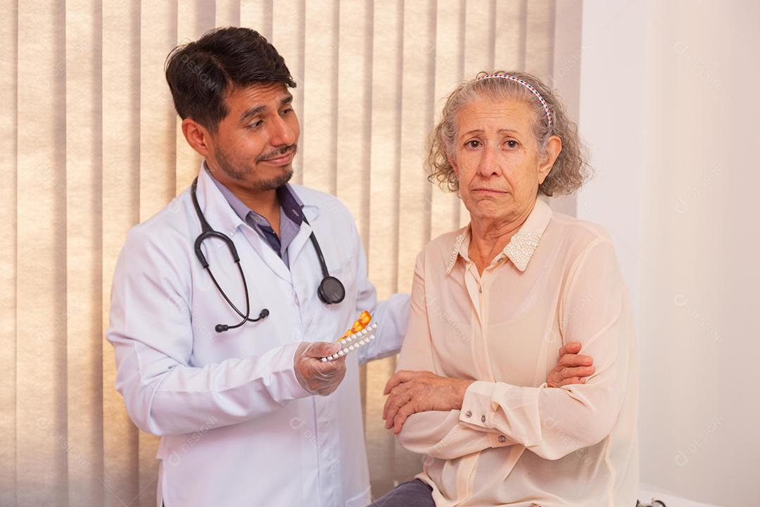 Mulher idosa com raiva por ter que tomar remédio. Médico tentando convencer a idosa a tomar remédio