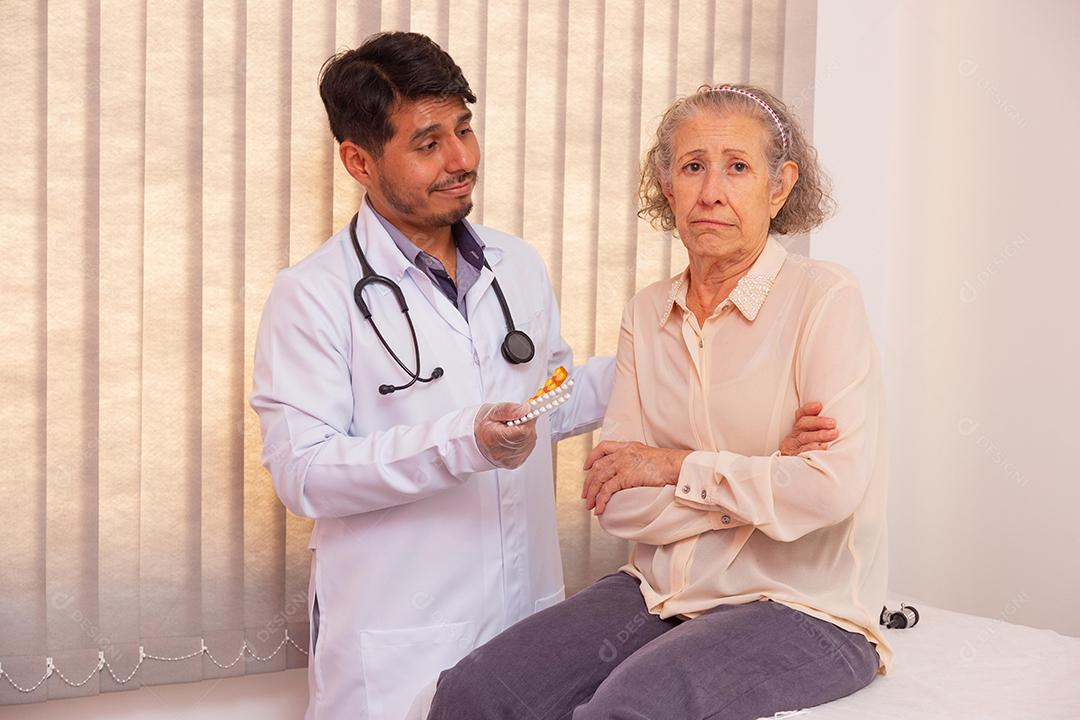 Mulher idosa com raiva por ter que tomar remédio. Médico tentando convencer a idosa a tomar remédio