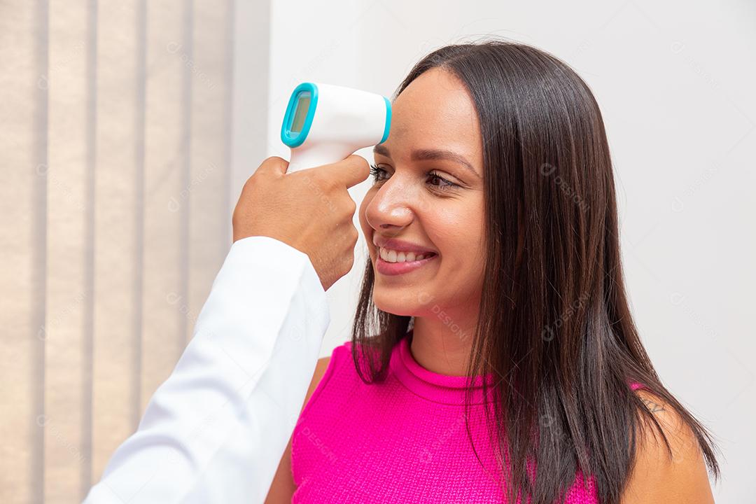 Conceito de medicina e cuidados de saúde. Médico com termômetro infravermelho sem contato fazendo triagem de temperatura, medindo febre com arma, digitalizando a testa de jovem na clínica