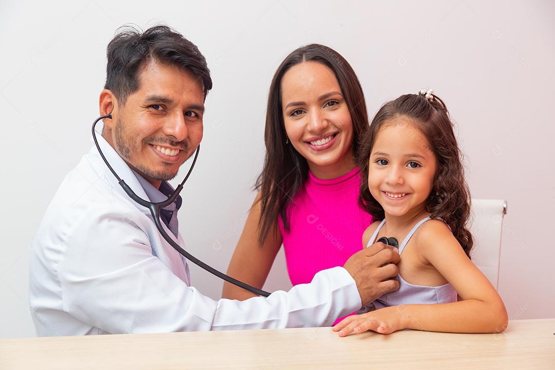 O pediatra masculino examina a menina com estetoscópio para verificar o pulmão e o coração. Mãe leva filha para pediatria.