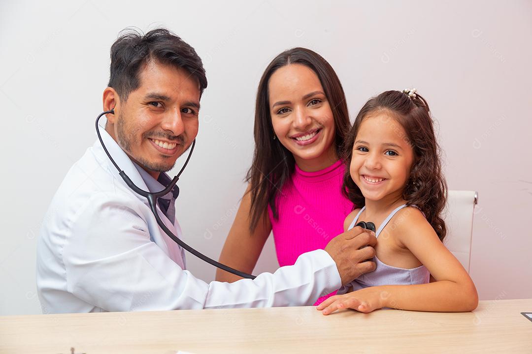 O pediatra masculino examina a menina com estetoscópio para verificar o pulmão e o coração. Mãe leva filha para pediatria.