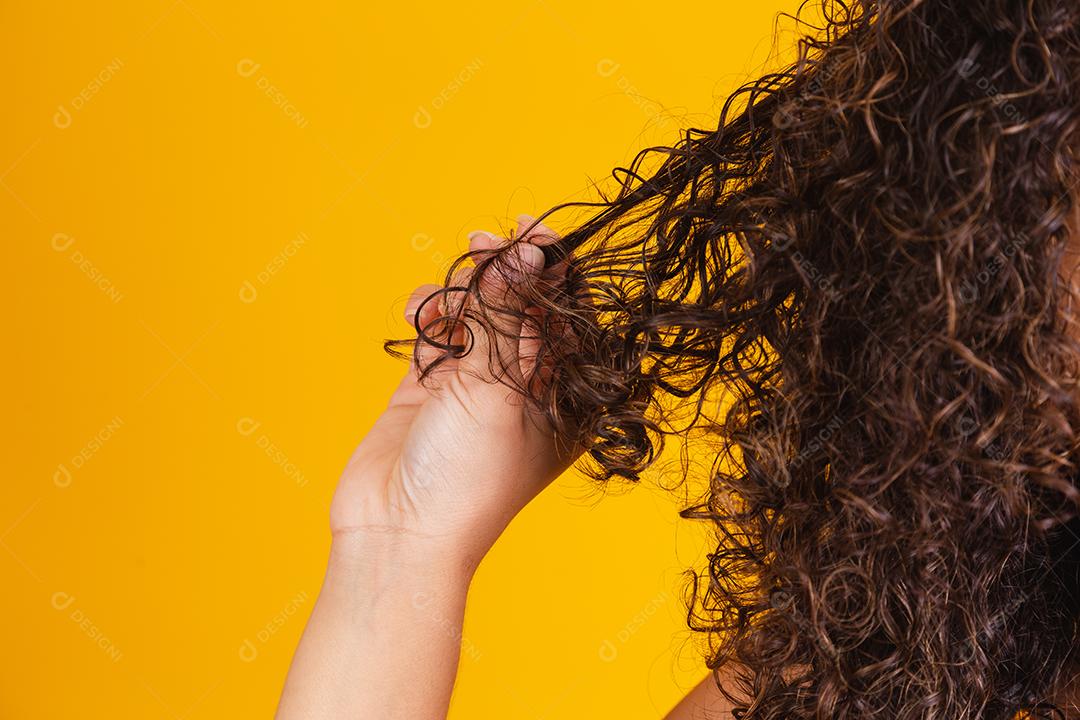 Mulher africana americana puxando uma mecha de cabelo. Cabelos cacheados em fundo amarelo.