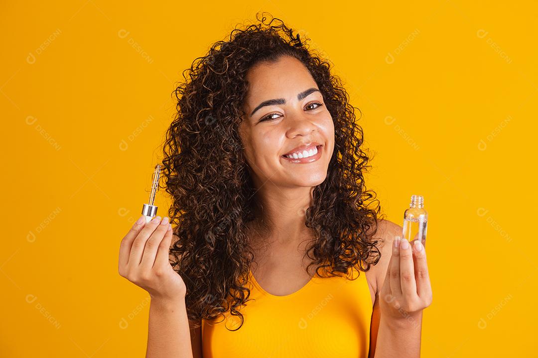 Tratamento reparador de pontas duplas. Mulher africana sorridente segurando um óleo nas mãos