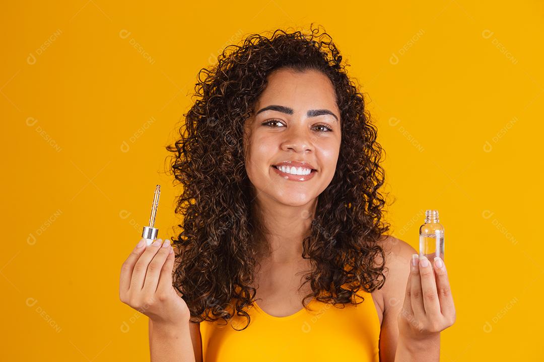 Tratamento reparador de pontas duplas. Mulher africana sorridente segurando um óleo nas mãos