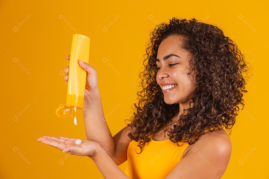 Linda mulher afro com cabelos cacheados aplicando creme no cabelo. Mulher afro com produto de cabelo na mão