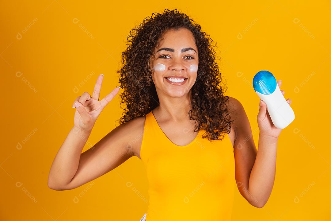 Jovem de maiô segurando um protetor solar. Jovem afro colocando protetor solar para proteger do sol