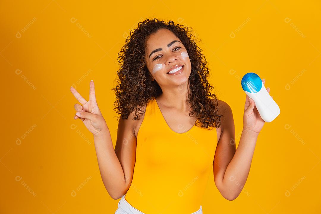 Jovem de maiô segurando um protetor solar. Jovem afro colocando protetor solar para proteger do sol