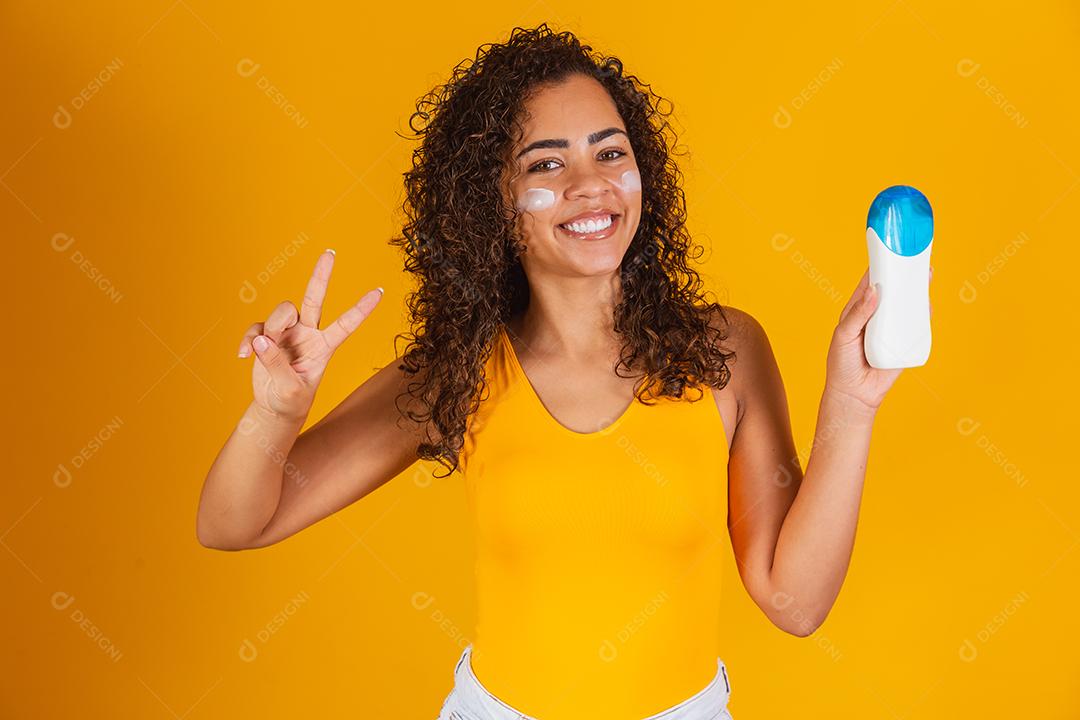 Jovem de maiô segurando um protetor solar. Jovem afro colocando protetor solar para proteger do sol