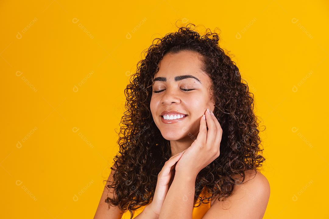 encantadora mulher afro com cabelos cacheados feliz com os olhos fechados sorrindo.