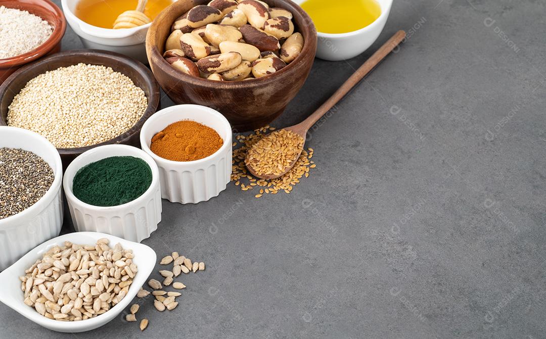 Super alimentos variados em colheres sobre fundo de pedra. Chia, quinoa, aveia, linhaça, mel, espirulina e outros.