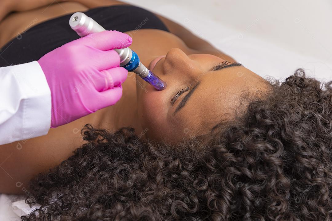 Jovem deitada na mesa do cosmetologista durante o procedimento de rejuvenescimento. Cosmetologista