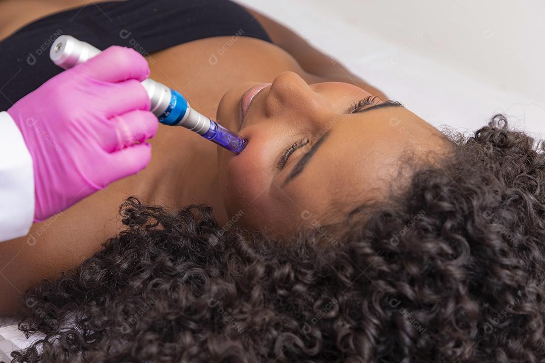 Jovem deitada na mesa do cosmetologista durante o procedimento de rejuvenescimento. Cosmetologista