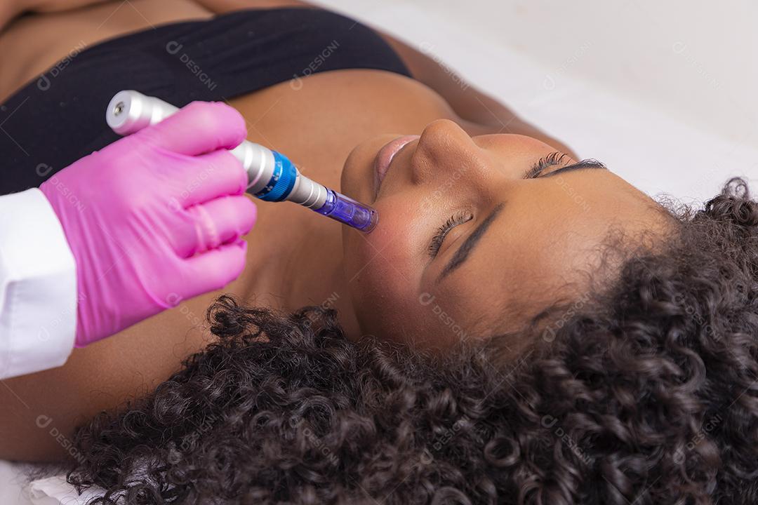 Jovem deitada na mesa do cosmetologista durante o procedimento de rejuvenescimento. Cosmetologista