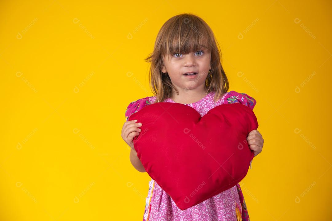 Menina caucasiana bonitinha segurando um coração de pelúcia vermelho. Sentimentos,