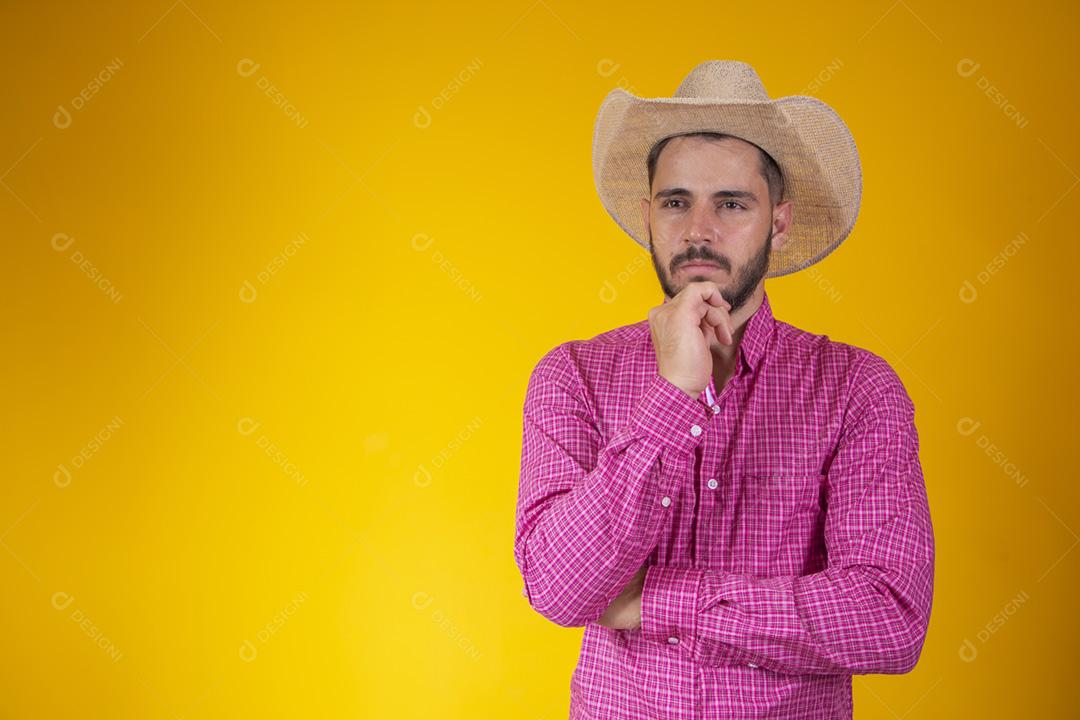 jovem agricultor serio com a mao no queixo olhando para a câmera no fundo amarelo