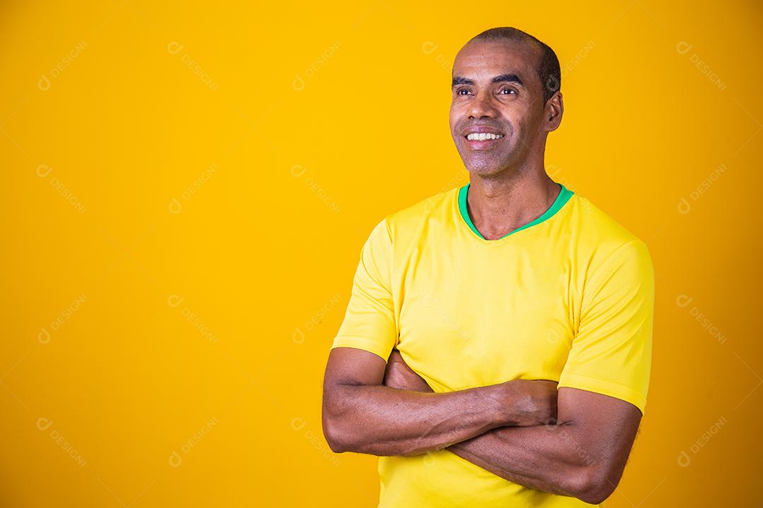 homem fã brasileiro com braços cruzados com camiseta amarela sorrindo