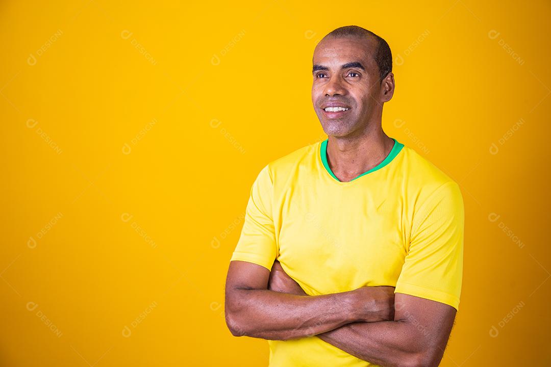 homem fã brasileiro com braços cruzados com camiseta amarela sorrindo