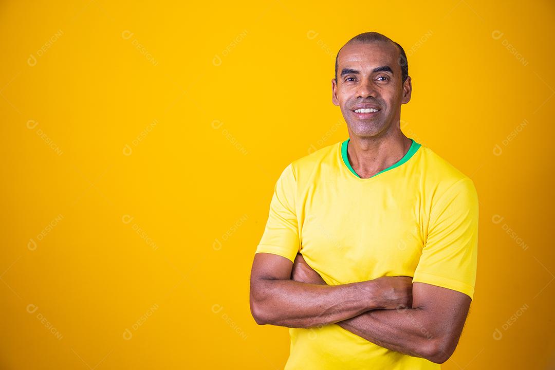 homem fã brasileiro com braços cruzados com camiseta amarela sorrindo