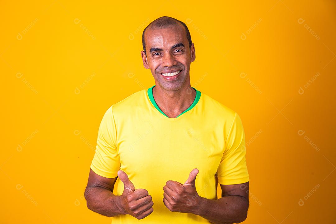 Fã de esportes brasileiro apoiando sua seleção nacional torcendo com os braços estendidos e polegares para cima vestindo a t-shirt