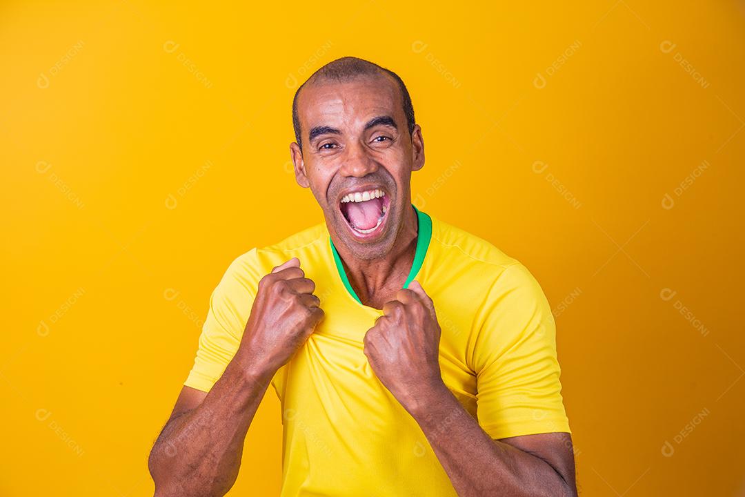 homem afro brasileiro bonito, fã brasileiro, brasil, copa do mundo 2022, punhos cerrados, gritando, torcendo, vibrando, gol.
