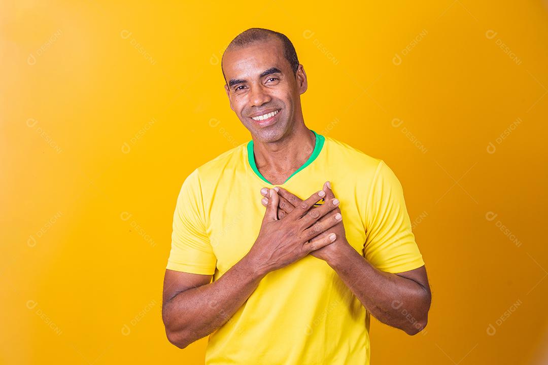 Homem moreno jovem colocando a mão no coração sobre fundo isolado amarelo