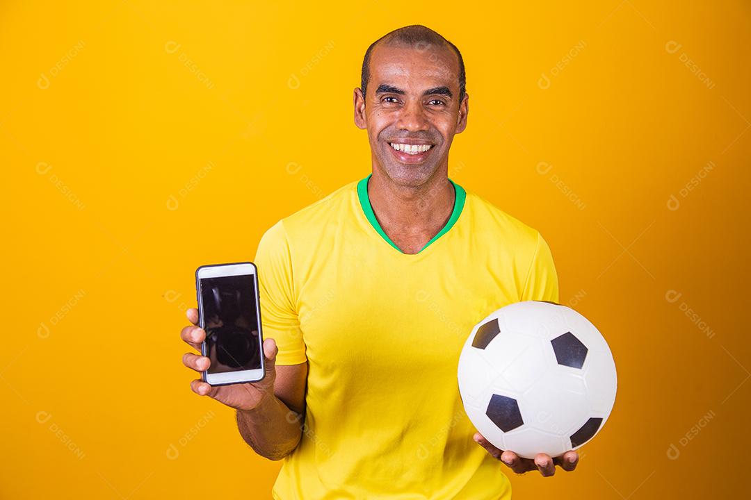 Homem fã brasileiro segurando um smartphone com tela em branco sobre fundo amarelo