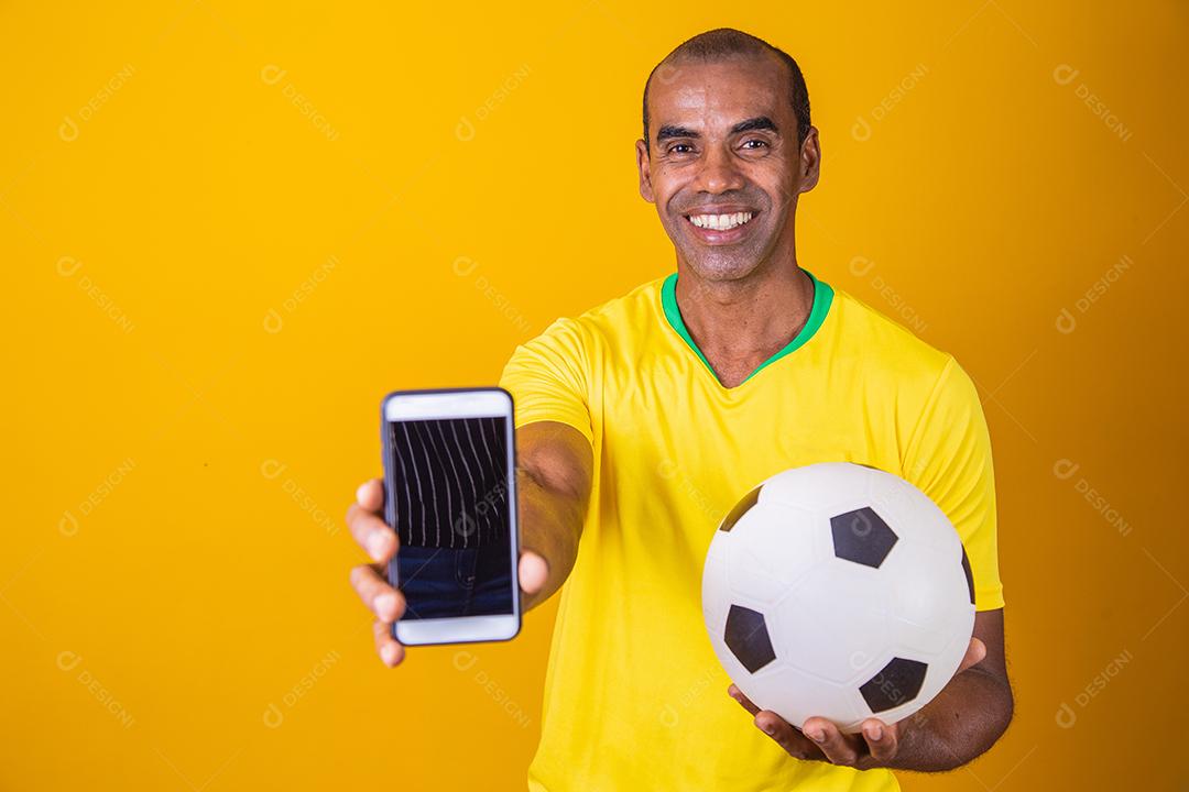 Homem fã brasileiro segurando um smartphone com tela em branco sobre fundo amarelo