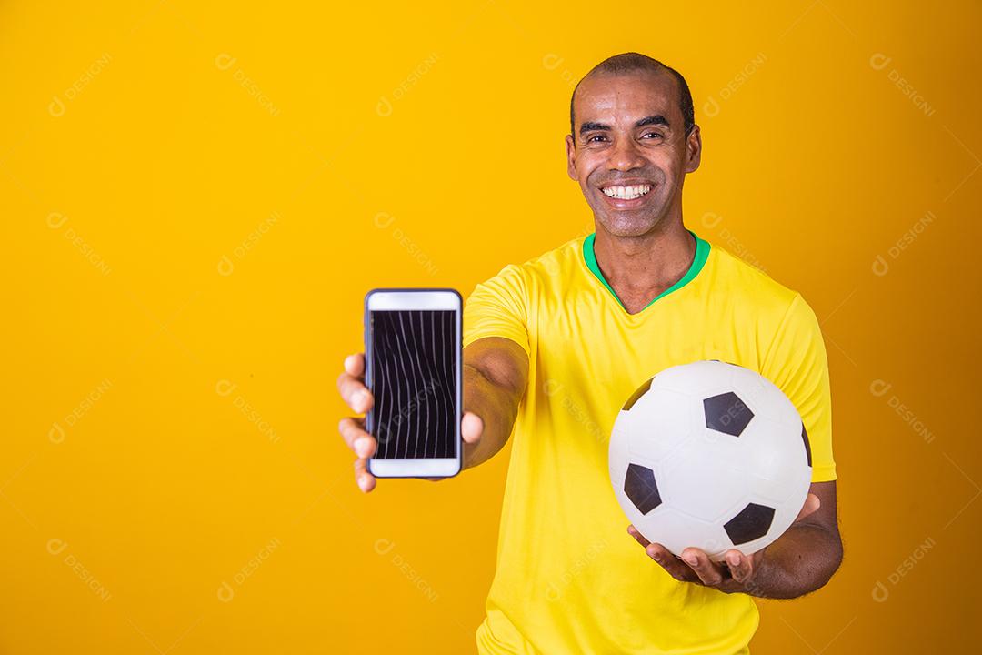 Homem fã brasileiro segurando um smartphone com tela em branco sobre fundo amarelo