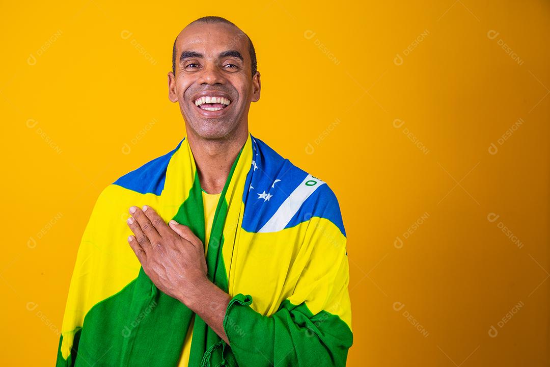 homem afro brasileiro bonito. Fã brasileiro. Copa do Mundo 2022, mão no peito cantando o hino nacional. Música brasileira. amada pátria. patriota.