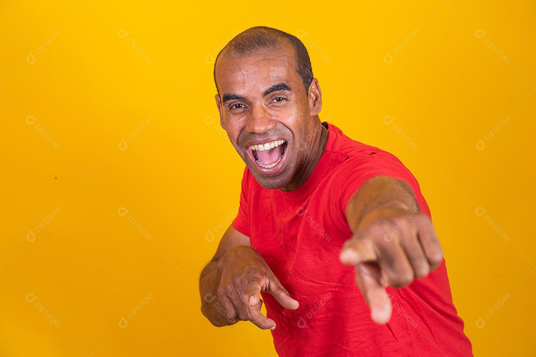 Homem negro positivo aponta o dedo indicador para a câmera, sorri alegremente e escolhe alguém isolado em fundo amarelo