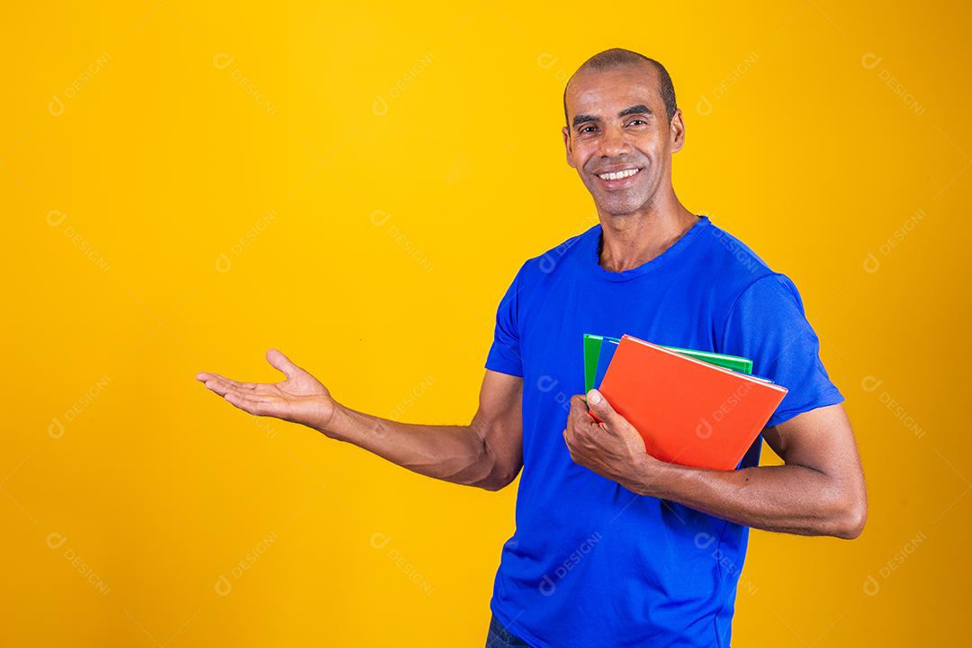 Homem estudante maduro com notebooks nos braços apontando para o lado