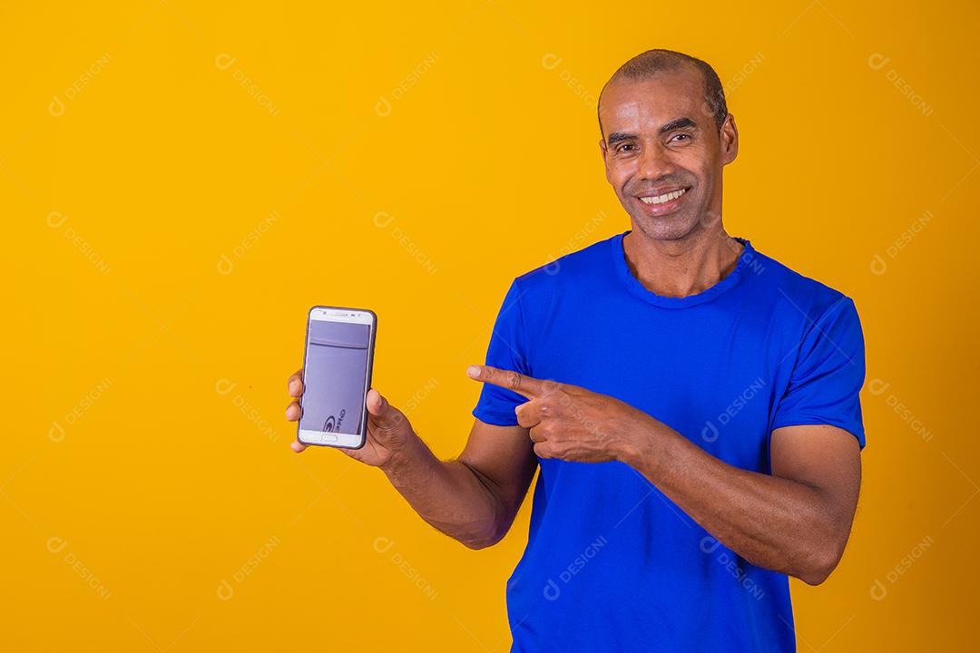 Homem afro-americano mostrando a tela do celular recomendando o aplicativo sorrindo para a câmera posando