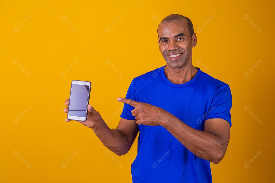 Homem afro-americano mostrando a tela do celular recomendando o aplicativo sorrindo para a câmera posando
