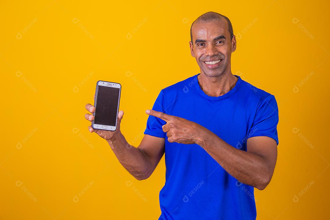 Homem afro-americano mostrando a tela do celular recomendando o aplicativo sorrindo para a câmera posando
