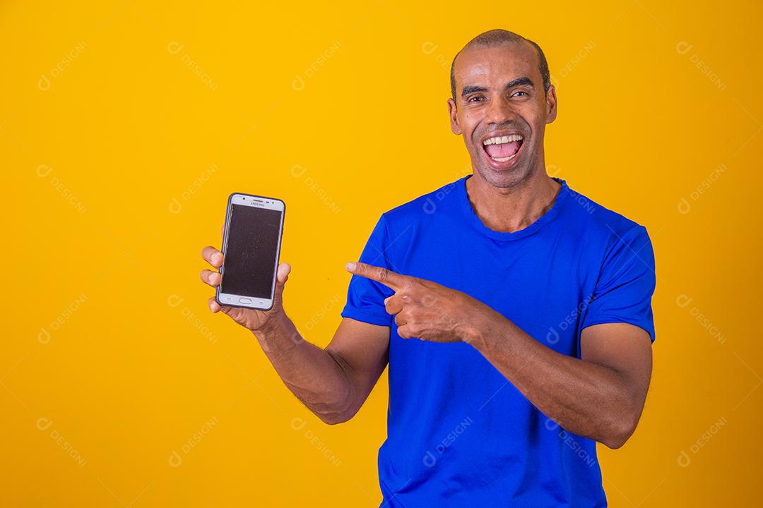 Homem afro-americano mostrando a tela do celular recomendando o aplicativo sorrindo para a câmera posando