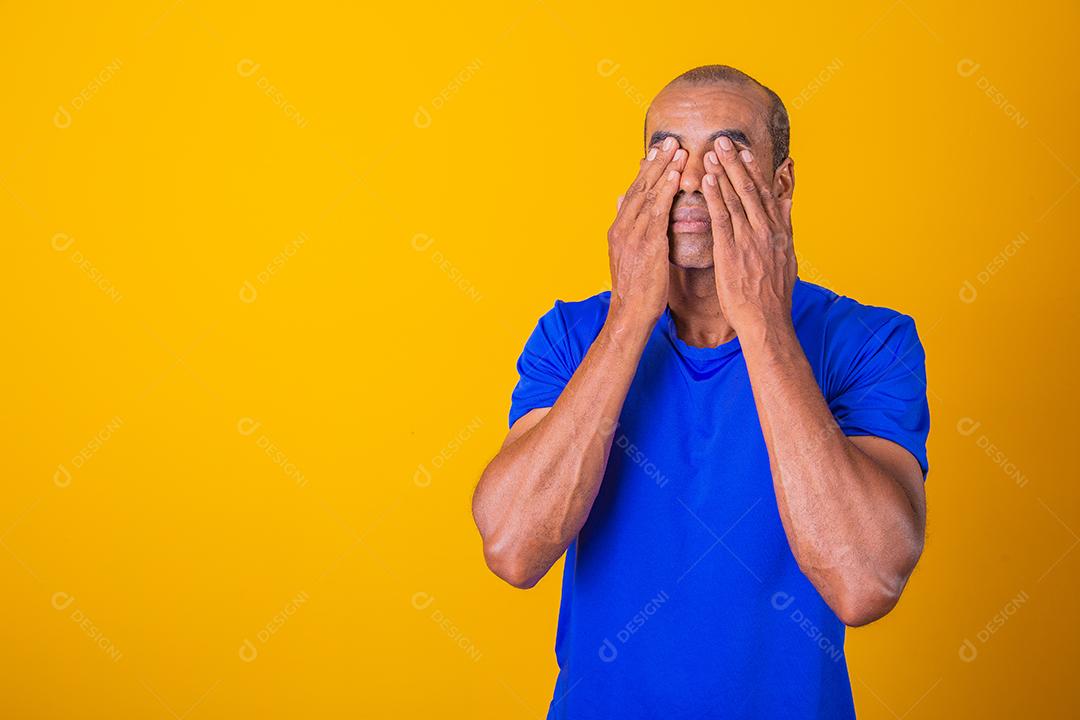 Homem afro cobrindo os olhos com as mãos no fundo amarelo