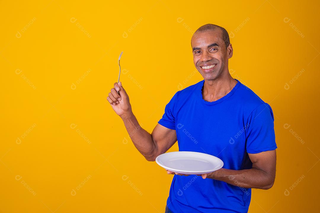 Homem afro segurando o prato vazio e garfo com isolado em fundo amarelo e faça o mock up.