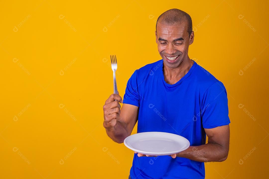 Homem afro segurando o prato vazio e garfo com isolado em fundo amarelo e faça o mock up.