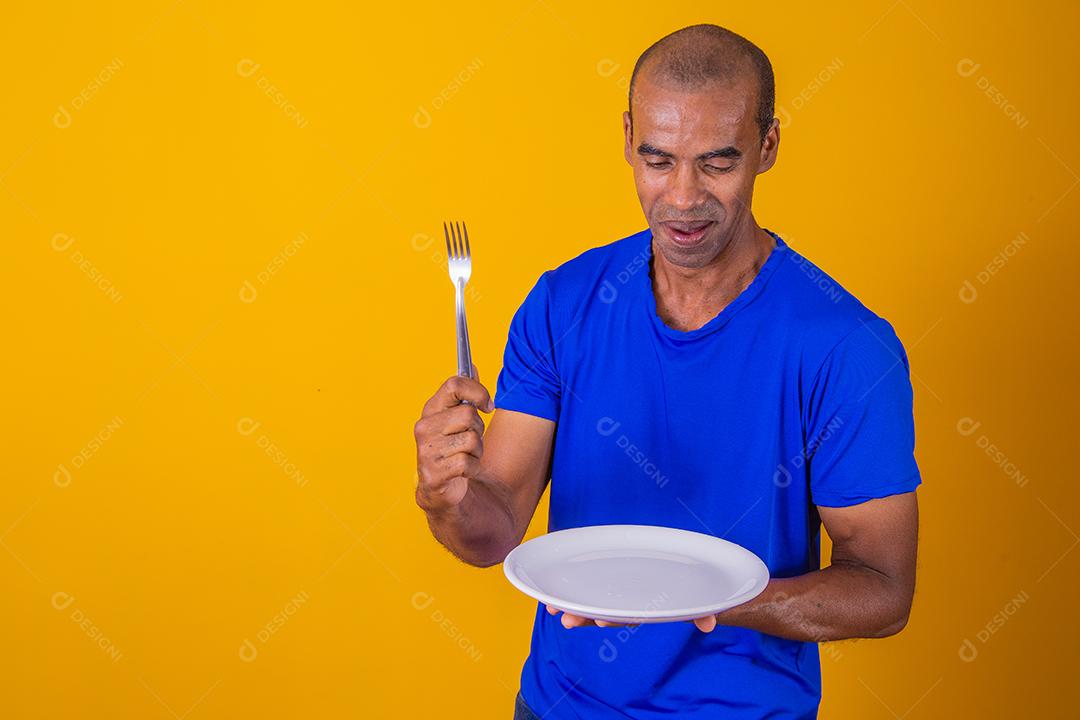 Homem afro segurando o prato vazio e garfo com isolado em fundo amarelo e faça o mock up.