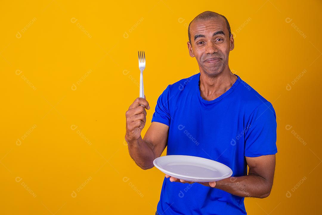Homem afro segurando o prato vazio e garfo com isolado em fundo amarelo e faça o mock up.
