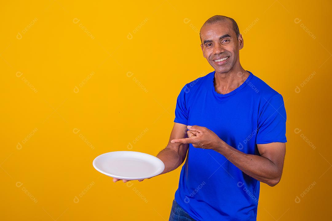 Homem afro segurando prato vazio em fundo amarelo