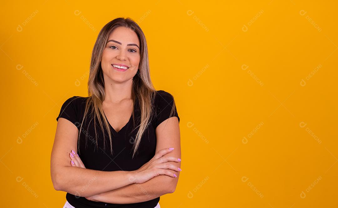 Mulher linda jovem de braços cruzados sorridente sobre um fundo isolado amarelo