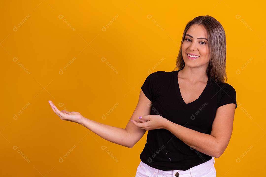 Mulher linda jovem apontando para lado sorridente sobre um fundo isolado amarelo