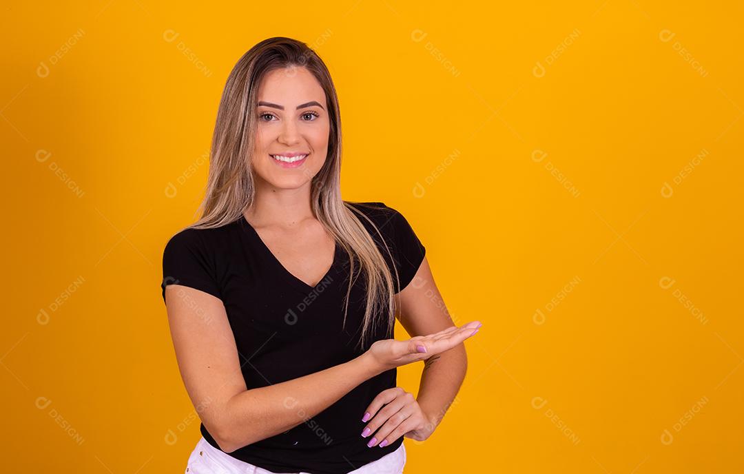 Mulher linda jovem apontando para lado sorridente sobre um fundo isolado amarelo