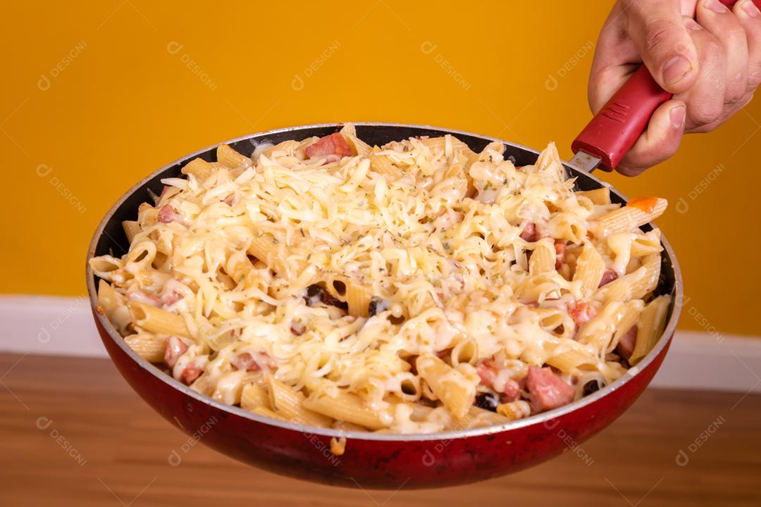 Mão segurando uma frigideira com macarrão e queijo derredido