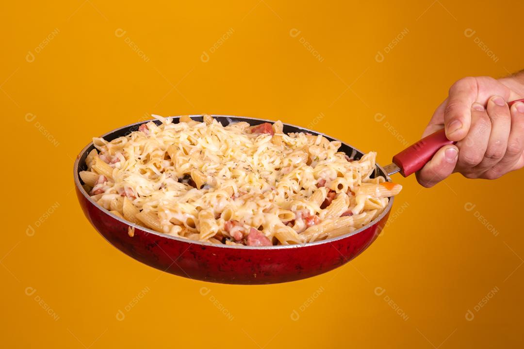 Mão segurando uma frigideira com macarrão e queijo derredido