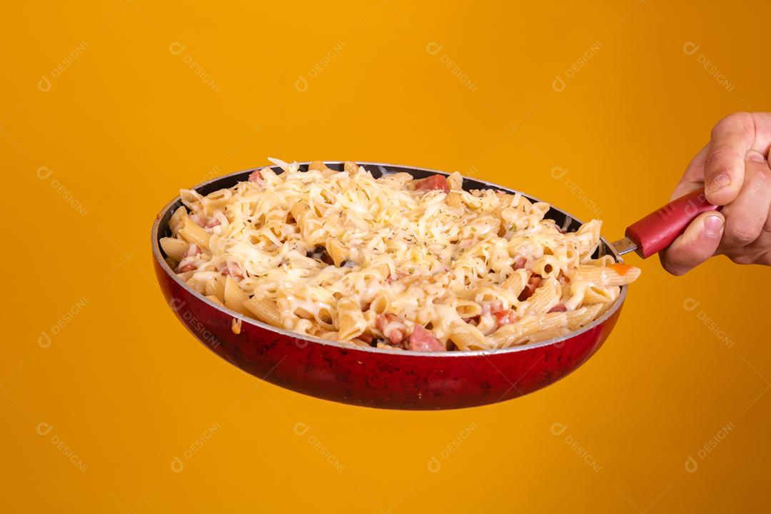 Mão segurando uma frigideira com macarrão e queijo derredido