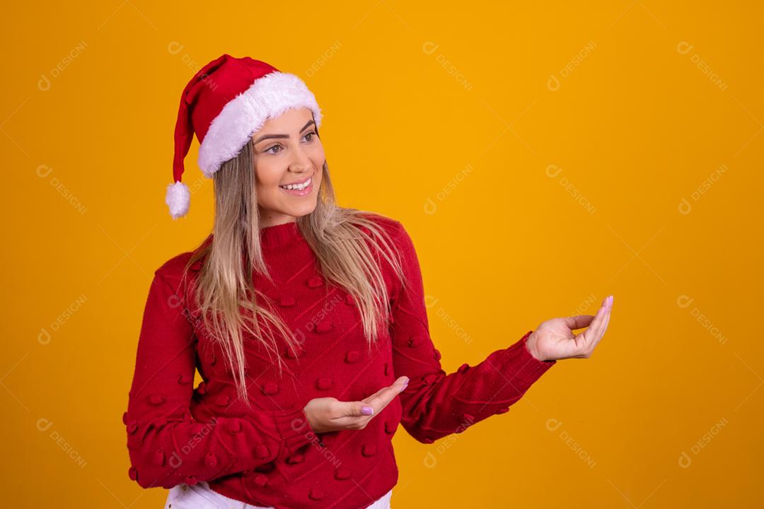 Mulher loira com um chapeu de papai noel em fundo amarelo