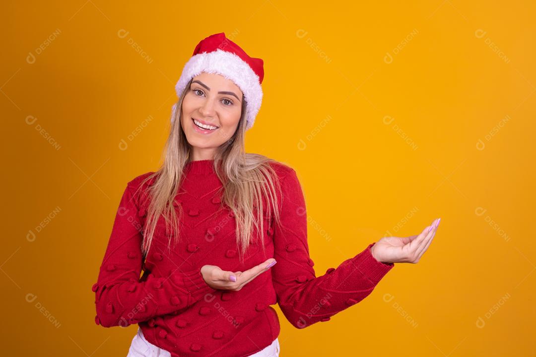 Mulher loira com um chapeu de papai noel em fundo amarelo