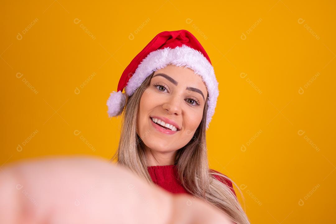 Mulher loira com um chapeu de papai noel em fundo amarelo